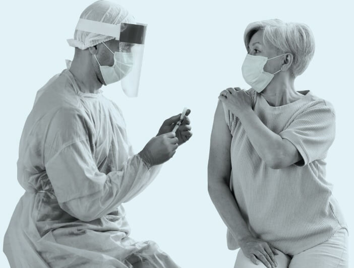 A person getting a vaccine shot from a healthcare worker with both wearing surgical masks